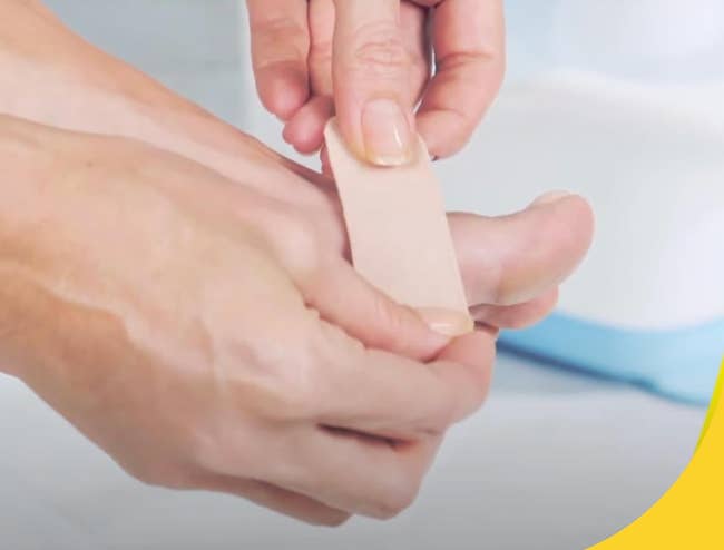 A close-up of a person's manus applying the moleskin pad to a foot