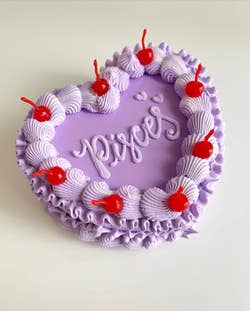 A lavender faux heart-shaped jewelry box lined with fake lavender icing and red cherries, with 