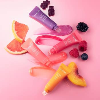 Variety of Laneige lip sleeping masks with fruit slices and berries on a pink surface, suggesting flavor inspiration for skincare shopping