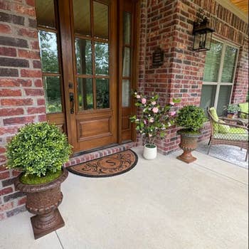 Front porch with two potted plants and a welcome mat outside a wooden door, suitable for enhancing home entryway aesthetics