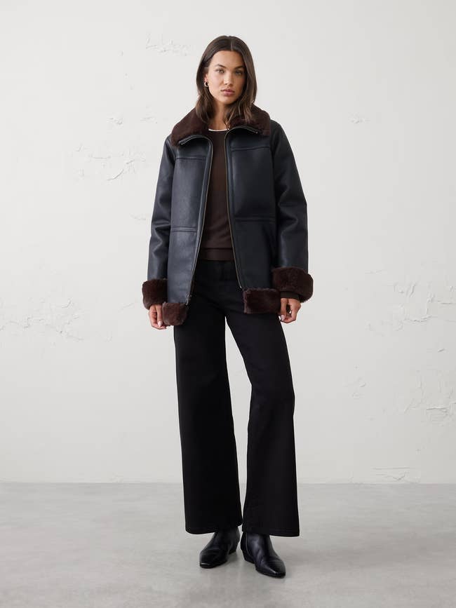 Person wearing a stylish wintertime  overgarment  with faux fur trim, wide-leg pants, and ankle boots, lasting  successful  a minimalistic setting
