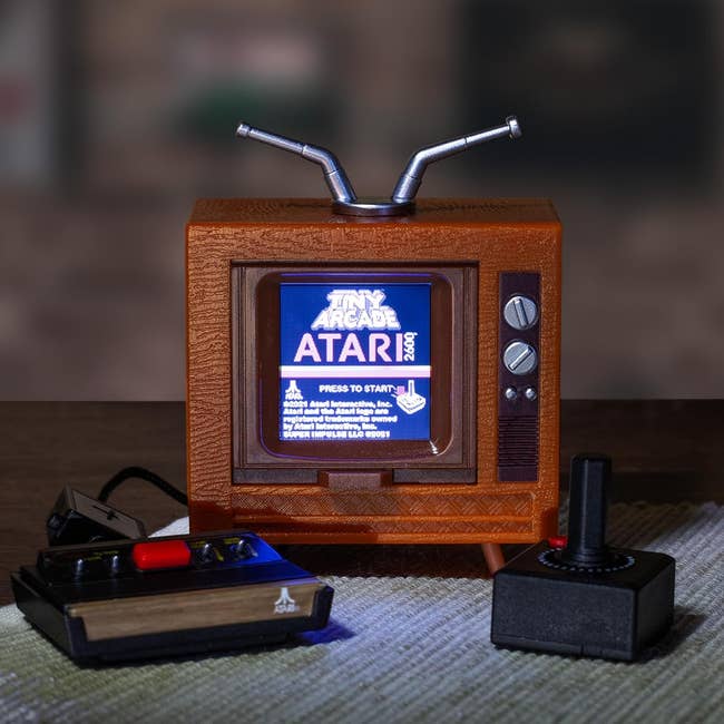 Miniature retro TV arcade instrumentality with joystick and crippled console, displaying Atari crippled paper connected screen