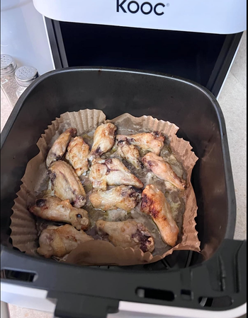 An air fryer open to show cooked food inside of a liner 