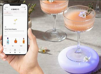  A model holding a phone app of recipes next to a cocktail resting on a lit up coaster 