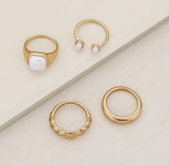 four rings: gold band, textured gold band, large square pearl, and open band with pearls on either side