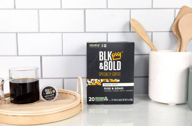 A BLK & BOLD coffee package on a kitchen counter with a cup of coffee and wooden utensils in a holder