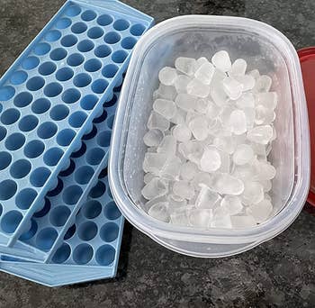 reviewer's three blue silicone ice trays next to a pile of tiny ice cubes 