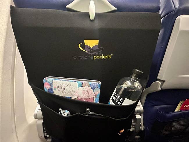 a reviewer's organizer on an airplane seat back with a bottle, iPad, and glasses inside