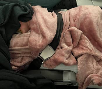 reviewer's child sleeping on the pink pillow under the pink blanket on a plane