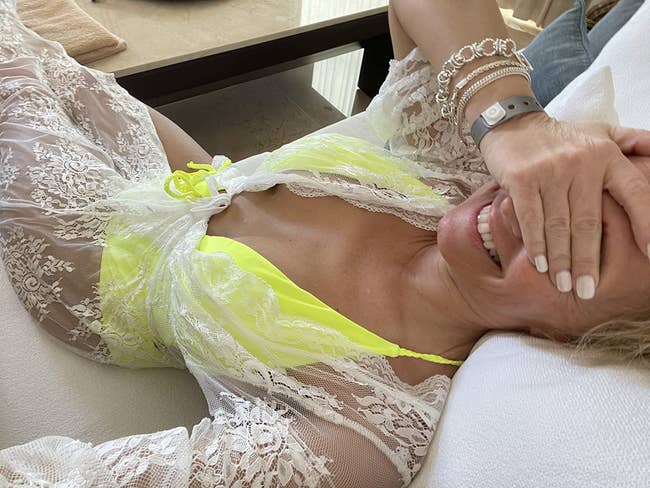 Person successful a lace cover-up implicit a swimsuit, reclining and smiling with manus covering portion of their face, featuring bracelets