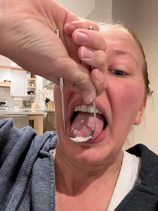 A reviewer demonstrates using a tongue scraper; it removes a mound of white gunk from their tongue