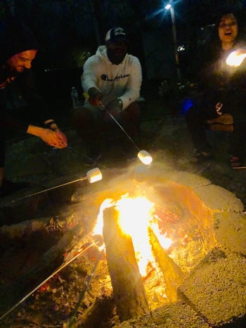 a bunch of people around a campfire using the extended sticks to roast marshmallows