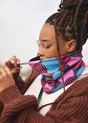 model wearing the blue, pink, and black neck gaiter while pulling the adjustable drawstring
