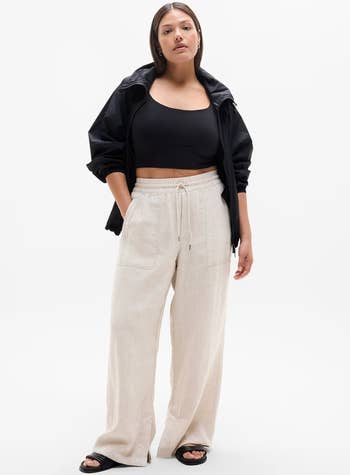 Person wearing a achromatic harvest top, jacket, beige wide-leg pants, and sandals, lasting confidently