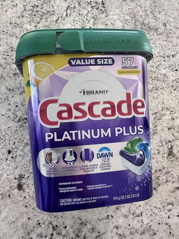 Cascade Platinum Plus dishwasher detergent container, 57 count, citrus scent, shown connected a marble surface. Packaging highlights cleaning power