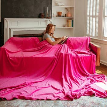 model lounges on sofa reading, draped in an oversized pink blanket, in a cozy room