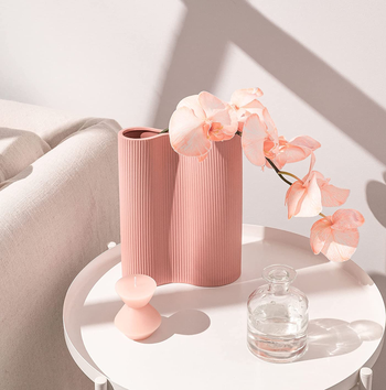the pink vase holding pink flowers on a small table filled with decorative items
