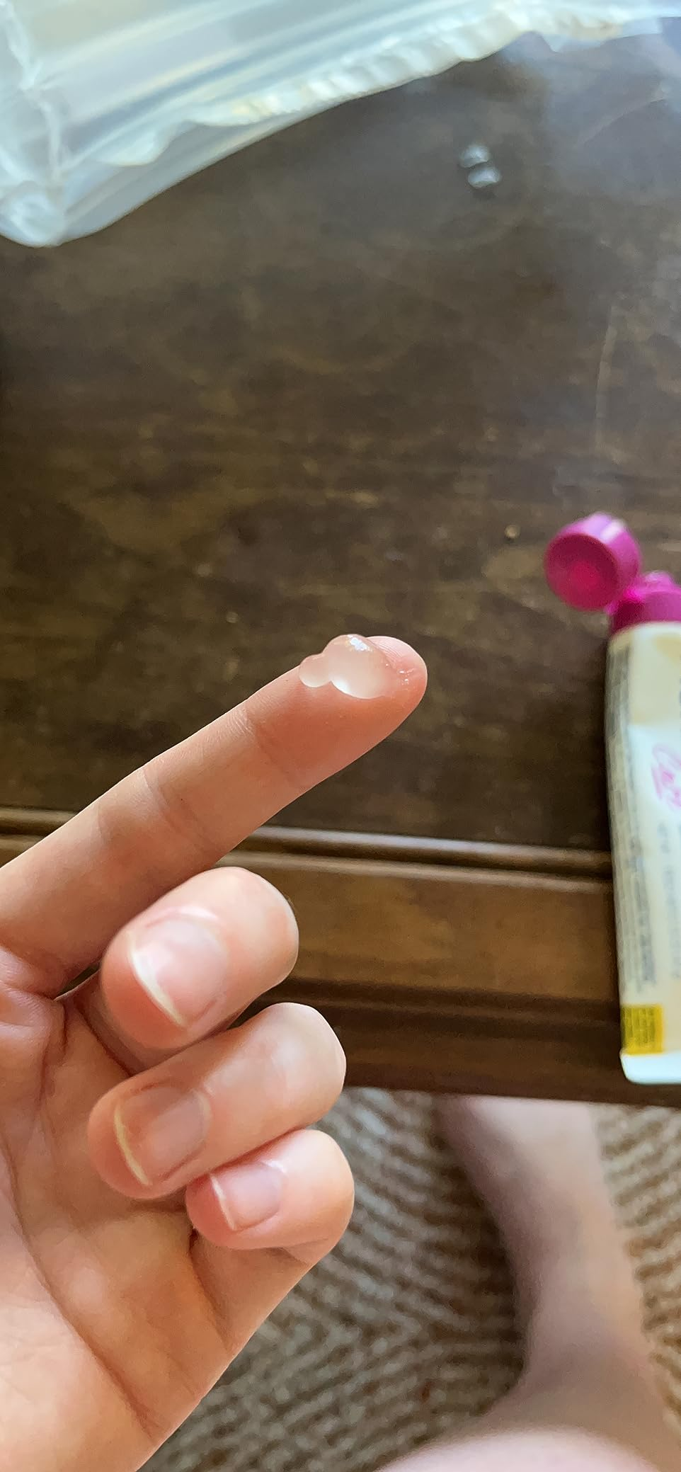 Person's digit  with a tiny  magnitude  of wide   gel connected  it, adjacent   an open, partially disposable   tube
