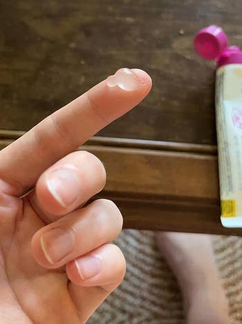 Person's digit with a tiny magnitude of wide gel connected it, adjacent an open, partially disposable tube