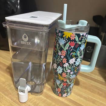 Floral-patterned tumbler with grip  and straw adjacent  to a Brita h2o  filter pitcher connected  a room  counter