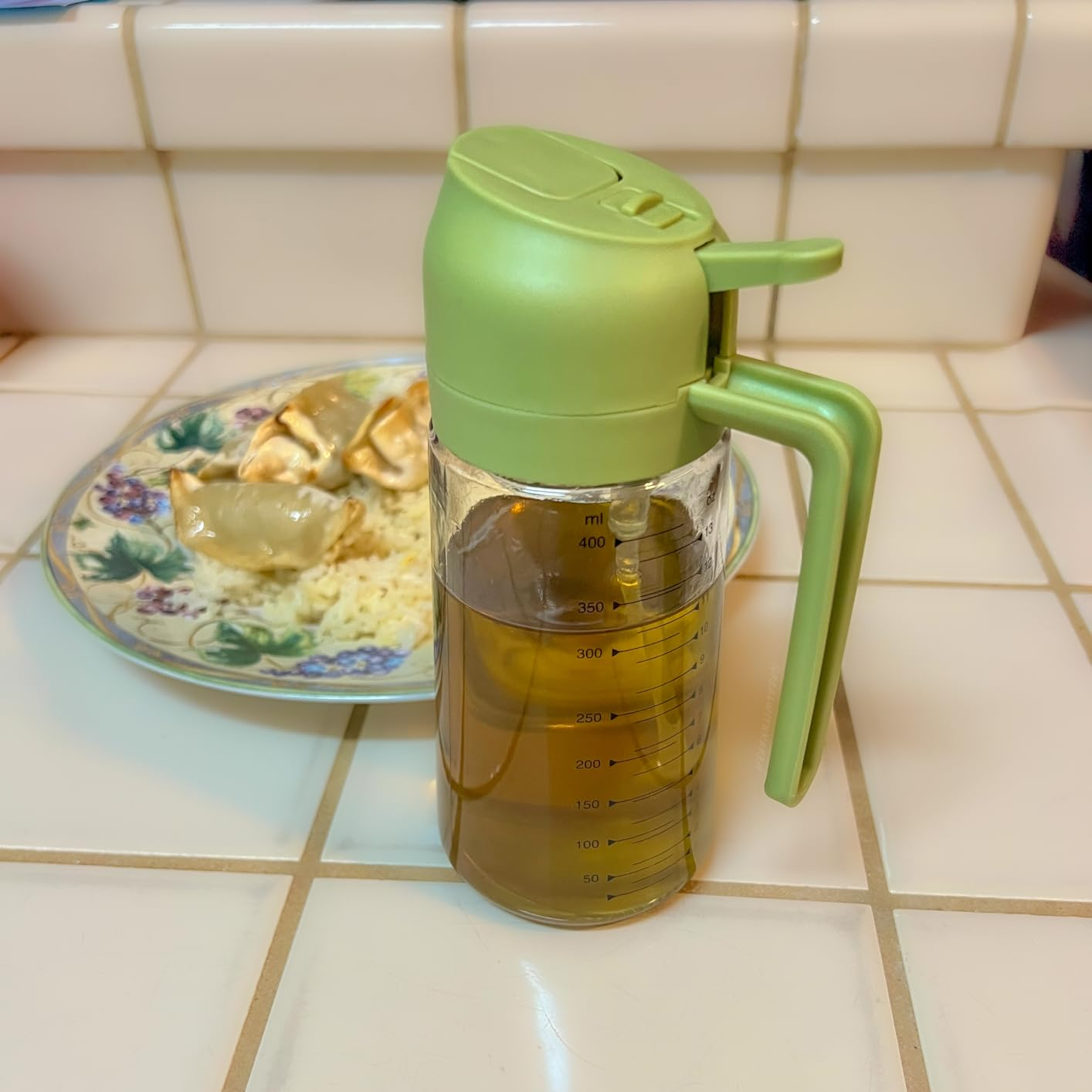 Olive lipid  dispenser connected  a tiled antagonistic  with a floral sheet  of dumplings and atom   successful  the background