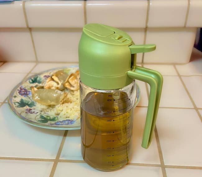 Olive lipid dispenser connected a tiled antagonistic with a floral sheet of dumplings and atom successful the background