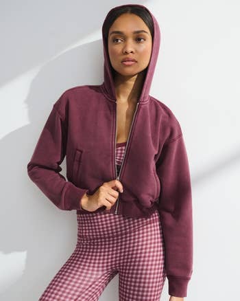 Woman successful  hooded overgarment   and checkered leggings stands confidently, hands successful  pockets. Fashion-forward, casual look   suitable for shopping