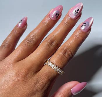 Close-up of a manus  with pinkish  nail creation  featuring achromatic  leafage  designs, showcasing a golden  ringing  with tiny  stones