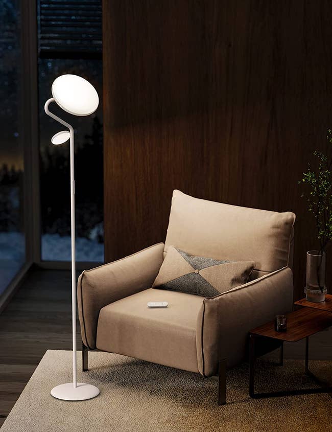 White skinny modern floor lamp with two circular light posts pointing down and up in front of a brown chair