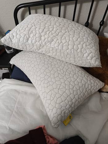 Two embossed-patterned pillows stacked connected  a furniture  with a metallic  frame, adjacent  to a bedside array  with a solid  of water