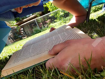 Reviewer reading a book in the grass with their face in the hole of the chair 
