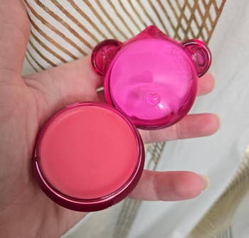 Round pinkish articulator balm successful a manus with a playful, bear-shaped pinkish case