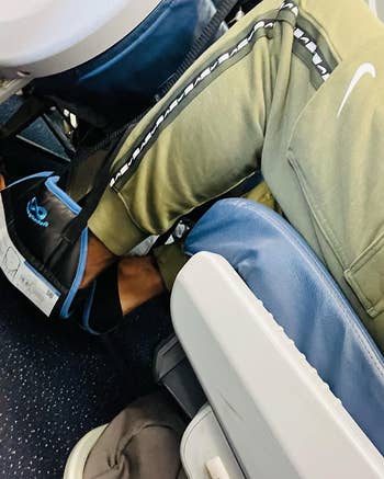 Person in a plane seat with a backpack between their legs, seemingly cramped for space