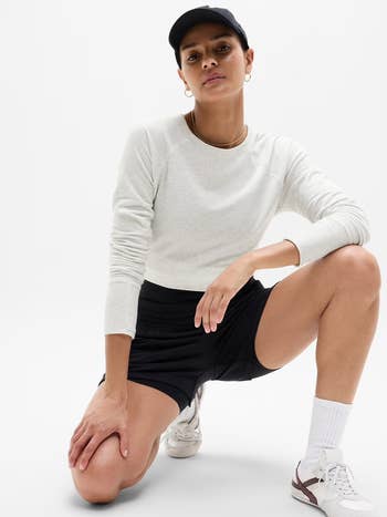 long-sleeve top, shorts, cap, and sneakers, posing confidently successful a sporty style