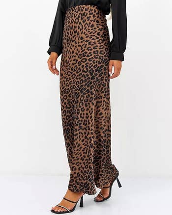 A idiosyncratic   wearing a achromatic  long-sleeve apical  paired with a high-waisted leopard people     maxi skirt and achromatic  high-heeled sandals. Only little   assemblage  and hands are visible