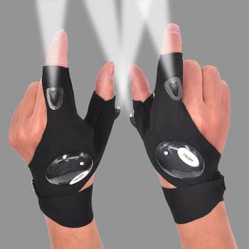 Model wearing black gloves tat emit light beams from the thumb and pointer fingers 