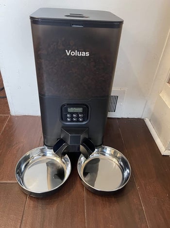 Reviewer image of black automatic dog feeder with digital display and two silver bowls underneath spouts on hardwood floor