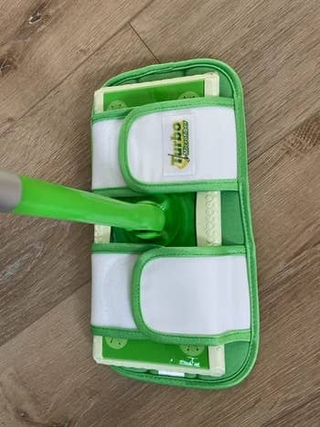 A green and white microfiber mop head on a wooden floor, suitable for cleaning and polishing surfaces