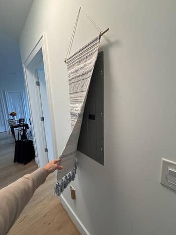 Wall tapestry used to conceal or decorate a utility panel in a hallway, with a hand adjusting it