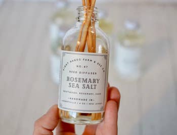 Model holding the bottle of rosemary sea salt oil with reeds in it