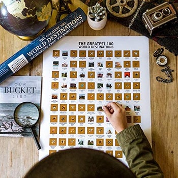 hand scratching off a destination on the greatest 100 world destinations scratch-off poster