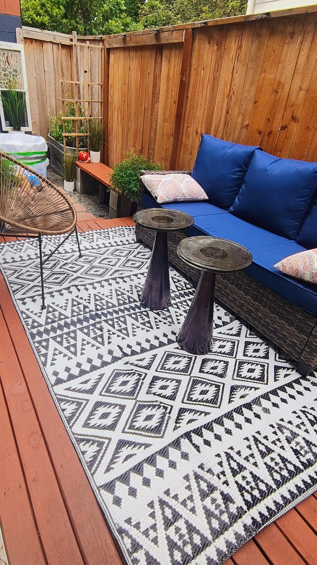 Outdoor patio with geometric-patterned rug, wicker sofa with plush cushions, woody  fencing, and tiny  tables. Cozy setup for relaxing oregon  entertaining