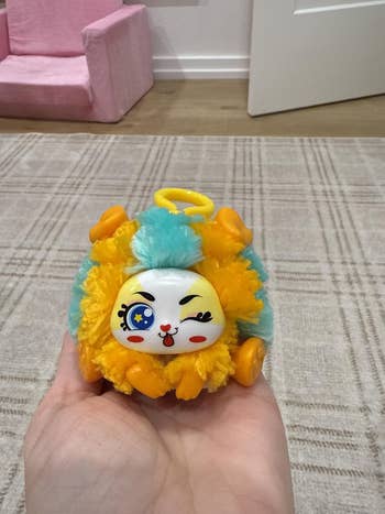 A manus  holding a round, fluffy artifact  with a winking face