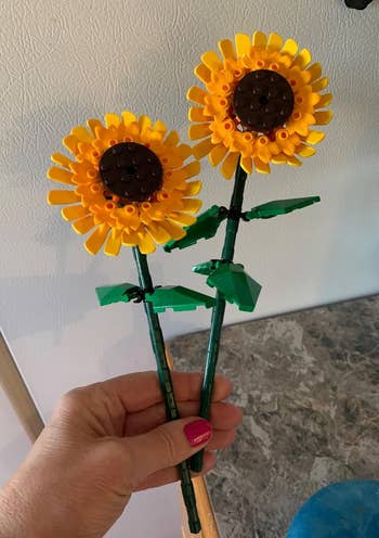 Two LEGO sunflowers with greenish  stems and leaves held successful  a hand