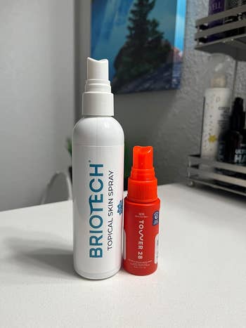 Reviewer's two skin care products, Briotech Topical Skin Spray and Tower 28 SOS, placed on a bathroom counter for size comparison