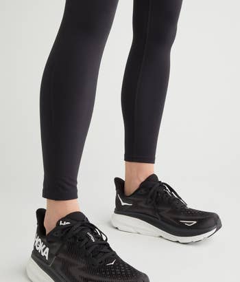 model wearing black athletic leggings and black HOKA running shoes