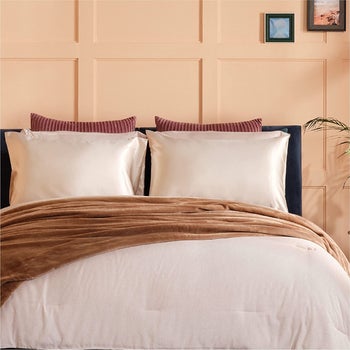 a bed with two pillows covered in beige satin pillowcases