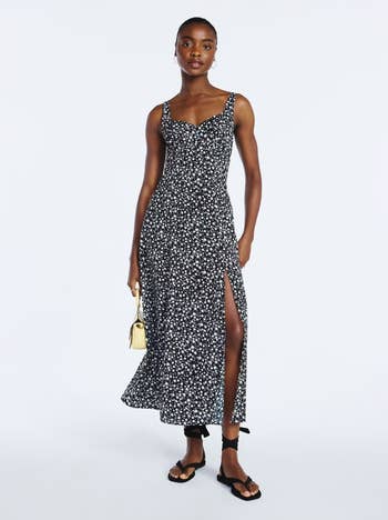 Person in a sleeveless floral dress with a thigh-high slit, holding a small purse