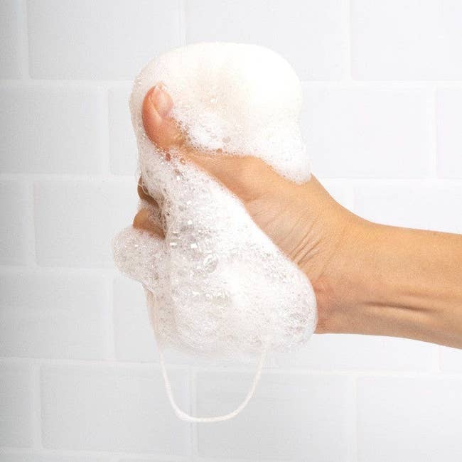 A hand squeezing the white sponge with lather coming out