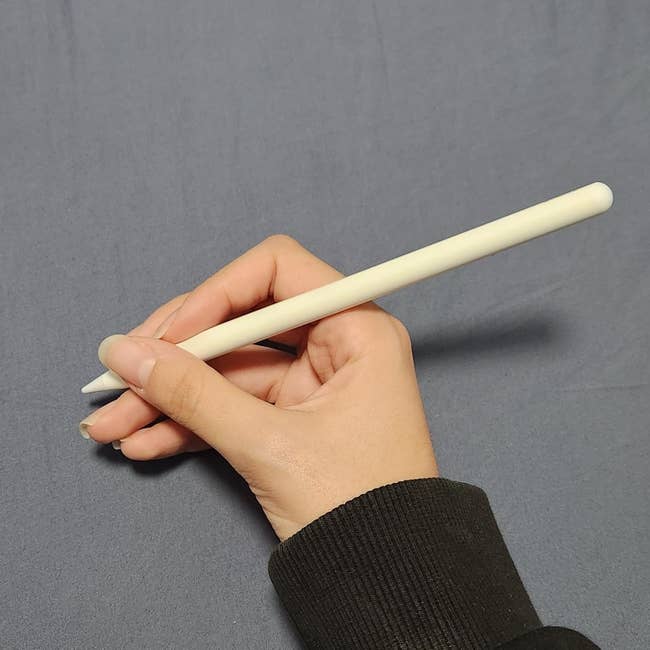A hand holding an Apple pencil above a plain surface